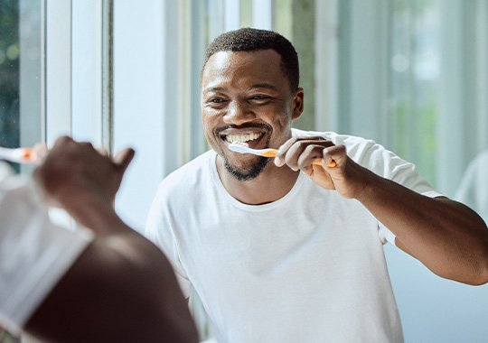 Man smiling while brushing his teeth