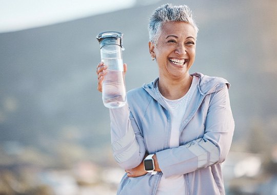 Woman smiling with water bottle on hike outside