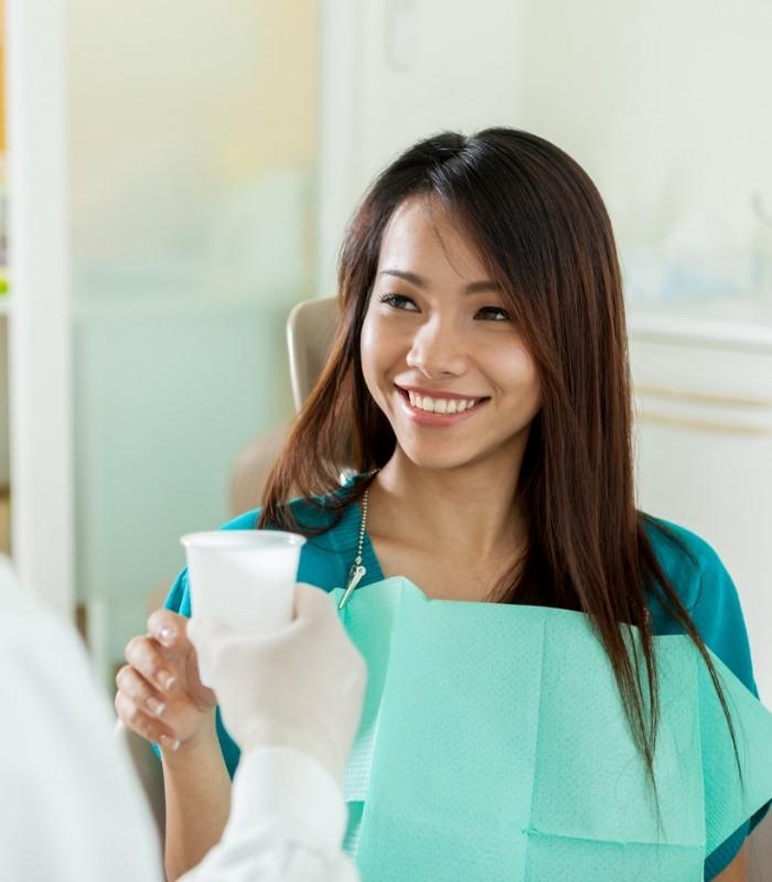Smiling woman in dental chair being handed a plastic cup of water