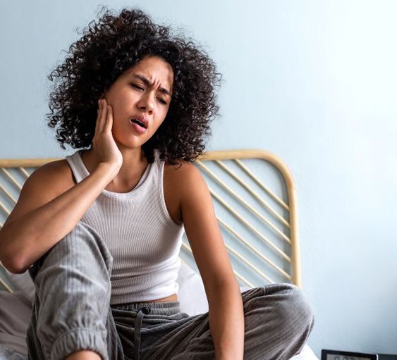 Woman sitting on her bed, suffering from jaw pain