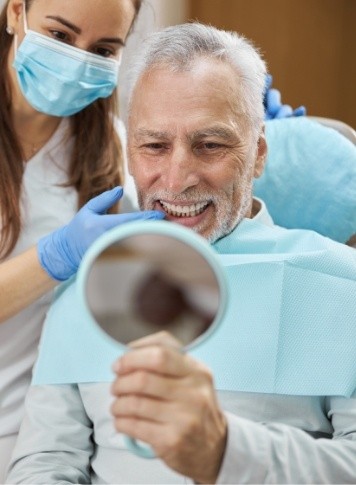 Senior man in dental chair admiring his smile in hand mirror