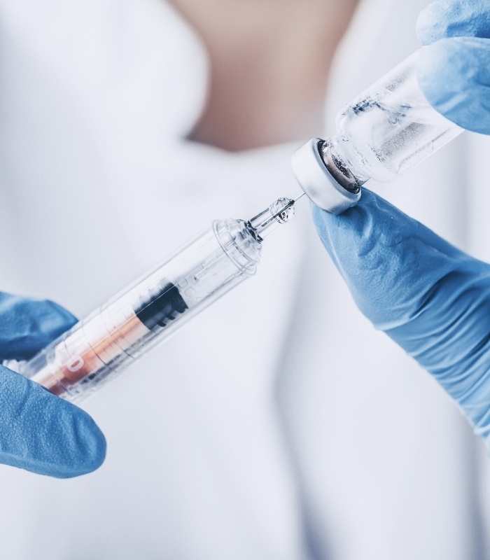 Dentist drawing syringe from vial of clear liquid