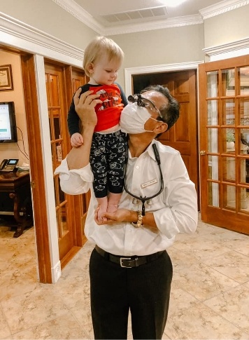 Doctor Lim in dental office holding a small child on his shoulder