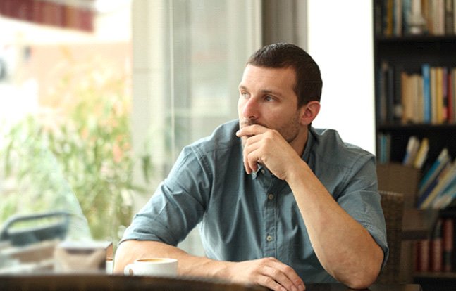 Man sitting at a table, wearing contemplative expression