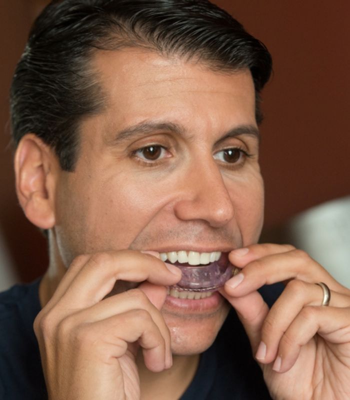 Man placing an oral appliance over his teeth for sleep apnea treatment