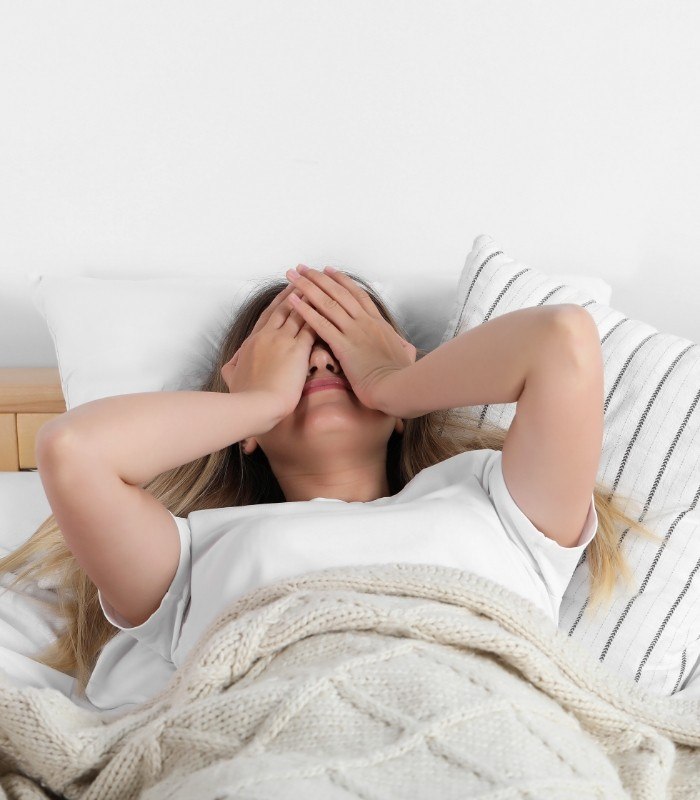 Woman lying in bed with her hands over her face