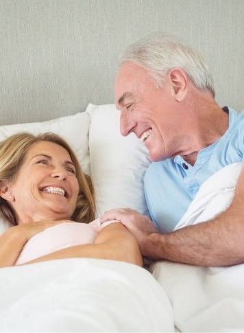 Senior man and woman laughing while laying in bed