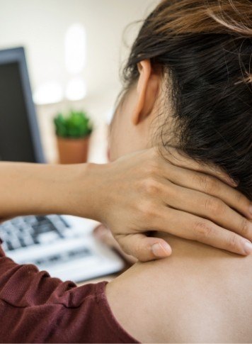 Woman sitting at desk rubbing the back of her neck