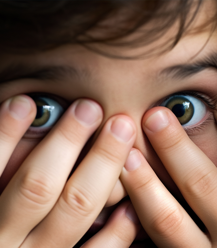 Close up of child covering their face with their eyes peeking through their fingers
