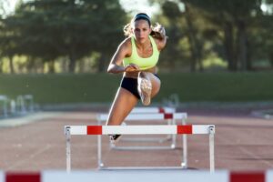 Female track athlete jumping over hurdles